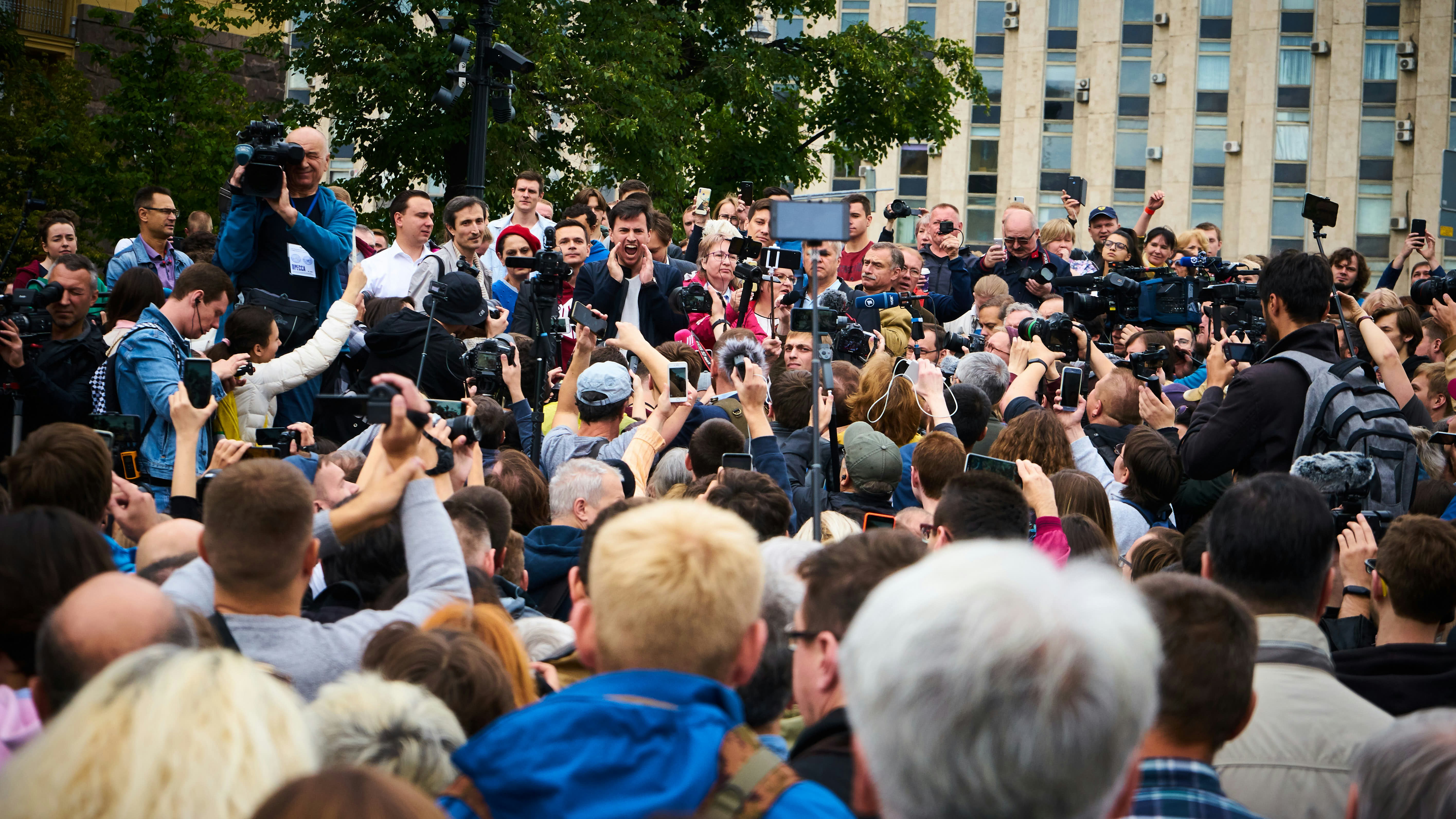 Press and public gathered around a speaker at a public policy event